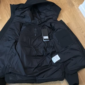 Canada goose McMillan black label - Säljer min  dunjacka från Canada Goose McMillan med huva och dragkedja som var lite för stor . Jackan har långa ärmar och en broderad logotyp på ärmen. Perfekt för kalla dagar.