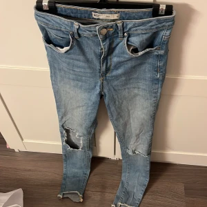 Tajta Blå jeans från Gina - Säljer ett par blå tajta jeans från Gina med slitna detaljer och en klassisk femficksdesign. Jeansen har en knappgylf och är i en skinny passform. 