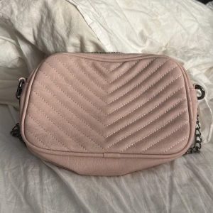 Rosa quiltad axelväska - Snygg rosa axelväska med quiltad design och kedjeaxelrem. Perfekt för att ge en stilren touch till din outfit. Väskan har en dragkedja upptill för säker förvaring av dina saker.