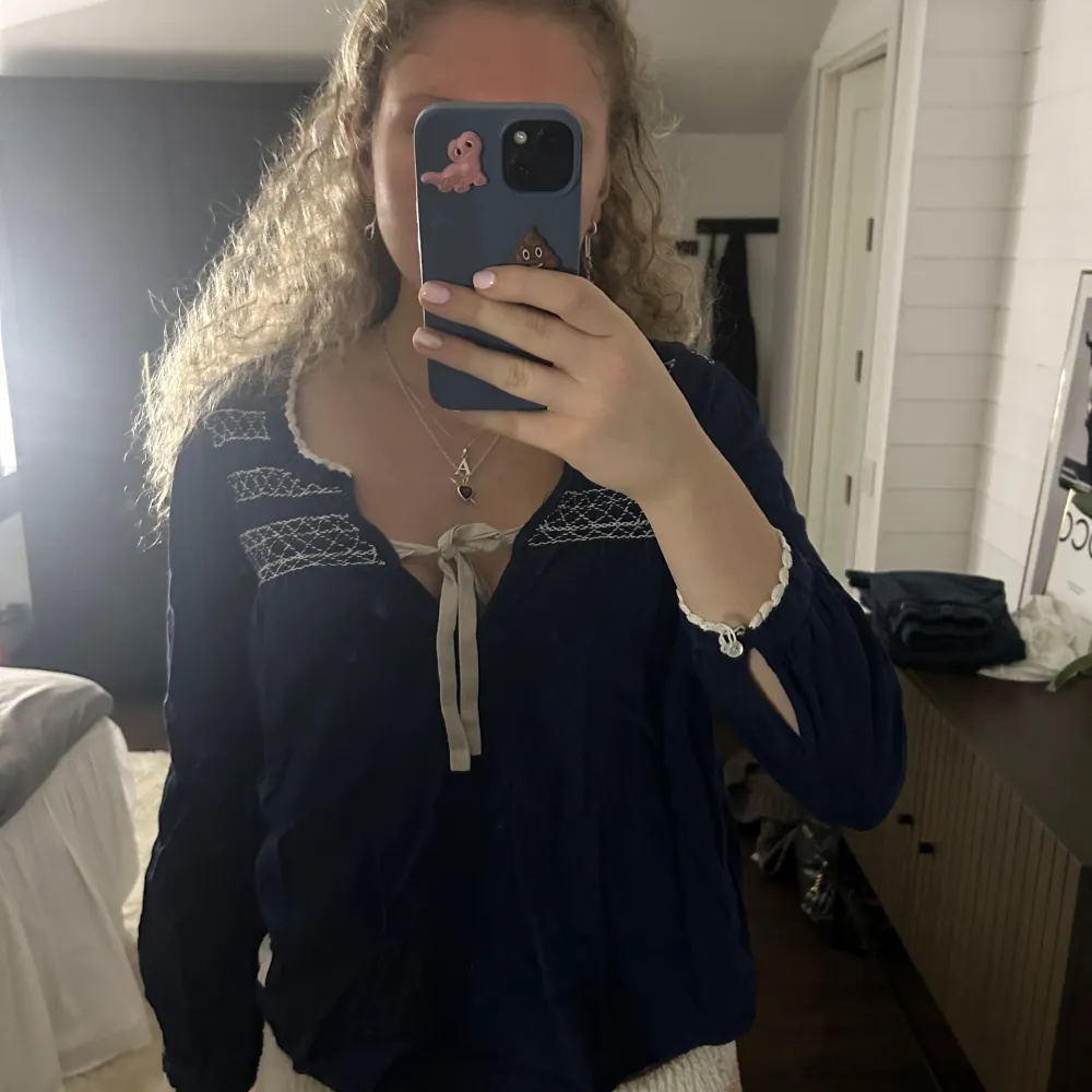 Säljer en söt mörkblå blus med spetsdetaljer och knytband framtill. Blusen har långa ärmar och en liten rosett vid ärmslutet. Perfekt för en stilren look.. Puserot.