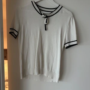 Vit kortärmad topp från Shein - Säljer en stilren vit topp från Shein med svarta detaljer. Toppen har korta ärmar och en knytning vid halsen. Perfekt för en chic och avslappnad look.