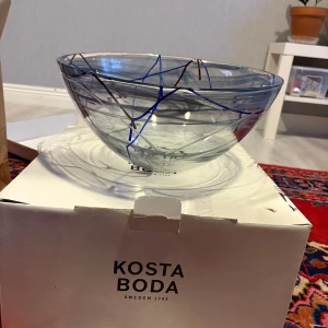 Glas skål från Kosta Boda - Elegant glas skål från Kosta Boda med abstrakt mönster i blått och rött. Perfekt som dekorativt inslag eller för servering. Skålen har en modern design med klara linjer och färger som ger ett stilrent intryck.