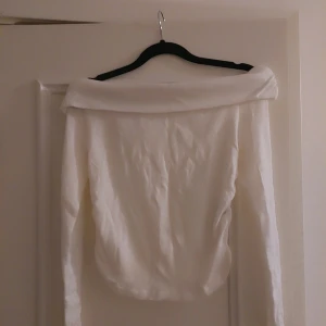 Vit offshoulder topp - Säljer en stilren vit offshoulder topp med långa ärmar. Perfekt för en chic och avslappnad look. Toppen är enkel att matcha med olika outfits.