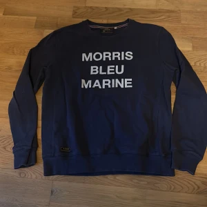 Blå tröja från Morris - Säljer en snygg blå tröja från Morris med texten 'MORRIS BLEU MARINE' på framsidan. Tröjan har långa ärmar och en rund halsringning. Perfekt för en avslappnad stil.