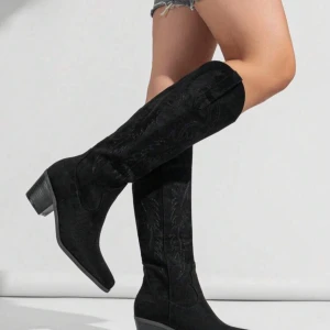 Svarta cowboy boots i mocka - Snygga svarta cowboy boots i mocka med dekorativa broderier. De har en låg klack och spetsig tå, vilket ger en klassisk look. Som helt nya och använt en gång inomhus perfekt för fester osv köpta för 800kr.