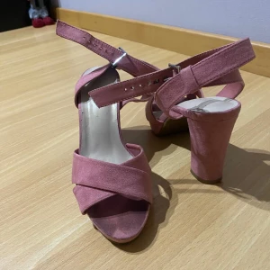 Rosa sandaler med klack - Snygga rosa sandaler med breda remmar och justerbart spänne runt ankeln. De har en stabil blockklack som ger extra höjd och stil. Perfekta för att lyfta din outfit med en touch av färg.