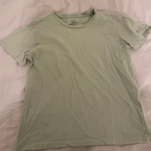 Grön t-shirt från 157 - Säljer en enkel och stilren grön t-shirt från 157 i storlek S. T-shirten är tillverkad i 100% bomull och har korta ärmar. Perfekt för en avslappnad look.