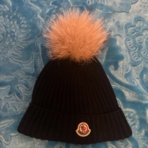 Moncler päls mössa - Hej, säljer moncler mössa som har en beige päls som är i gott skick utan några skador och är såklart äkta. Den är i storleken L men kan passa mindre storlekar då den inte är så stor i storleken.