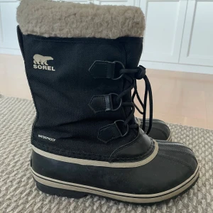 Svarta vinterstövlar från Sorel - Säljer ett par svarta vinterstövlar från Sorel med snörning och varm foder. Stövlarna är vattentäta och har en robust sula för bra grepp. Perfekta för kalla och snöiga dagar.