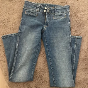 Blå bootcut jeans från H&M - Säljer ett par blå bootcut jeans från H&M med justerbar låg midja. Jeansen har en klassisk femficksdesign och knappar fram. Perfekta för en avslappnad stil. Dem har lite detaljer på byxorna som jag visade. 90kr + frakt