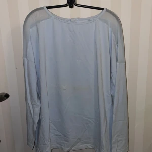 Ljusblå långärmad topp med meshdetaljer - Snygg ljusblå topp med långa ärmar och meshdetaljer på axlarna. Toppen har en dragkedja i ryggen för en stilren look. Perfekt för en avslappnad men trendig stil.