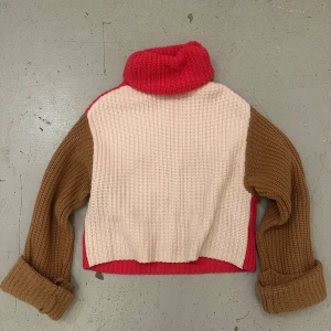 Flerfärgad stickad tröja - Säljer en unik flerfärgad stickad tröja i ullblandning. Tröjan har en hög krage och långa ärmar i brunt, med en beige kropp och röda detaljer. Perfekt för kyliga dagar!