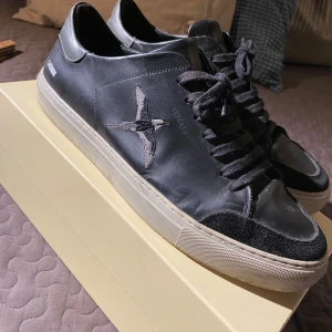 Svarta sneakers från Axel Arigato - Snygga svarta sneakers från Axel Arigato med en stilren design. Skorna har en fågelbrodering på sidan och är tillverkade i skinn med snörning framtill. Perfekta för en avslappnad stil. Box och kvitto finns kvar. Hör gärna av dig om du har några frågor om pris ,storlek mm. 