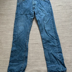 Blå jeans från Levi's 501 - Säljer ett par klassiska blå jeans från Levi's i bra skick. W34/L34 de har en straight passform och är tillverkade i slitstarkt denim. Perfekta för både vardag och avslappnade tillfällen. Märkta med Levi's ikoniska läderpatch på baksidan. Passar perfekt till höst och vår!