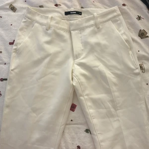 Vita lågmidjade kostymbyxor från Bikbok - Säljer ett par eleganta vita kostymbyxor från Bikbok. De är lågmidjade med en klassisk straight passform och slits vid slutet av benen. Perfekta för både vardag och festliga tillfällen. Byxorna har diskreta fickor och hällor för bälte. Materialet känns lyxigt och är av hög kvalitet. De är använda en gång och är i modellen vera!