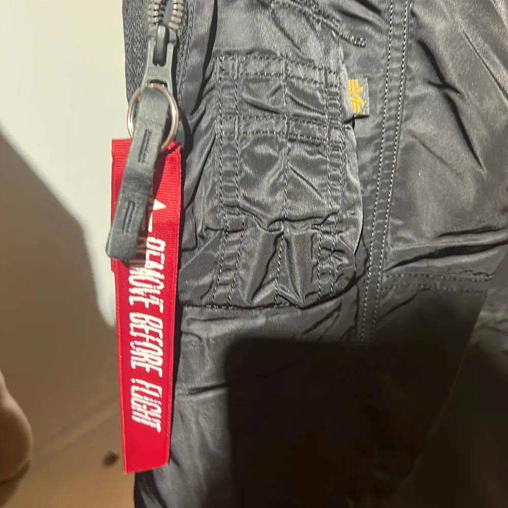 Säljer en svart jacka från Alpha Industries i storlek L. Den har en orange insida och en avtagbar huva med fuskpäls. Jackan har dragkedja och flera fickor, samt en cool 'Remove Before Flight'-detalj. Perfekt för höst och vinter!. Jackor.