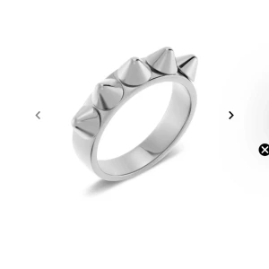 Silvrig ring med nitar - Cool och edgy silvrig ring med spetsiga nitar runtom. Perfekt för att ge din outfit en tuff touch. Passar både till vardags och festliga tillfällen. Tillverkad i ett hållbart material som håller länge.