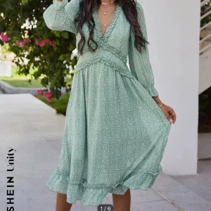 Grön blommig klänning från SHEIN - Superfin grön klänning från SHEIN med små blommor. Den har en omlott-design och volangdetaljer längst ner. Perfekt för vår och sommar! Klänningen har långa ärmar och en v-ringad hals. 