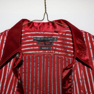 Röd och vit randig skjorta från BLY03 - Snygg röd och vit randig skjorta från BLY03 i ett glansigt material. Skjortan har långa ärmar och knappar framtill. Perfekt för en festlig kväll eller en stilfull vardag. Den har en klassisk krage och en elegant look som verkligen sticker ut.