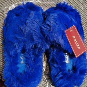 Blå fluffiga tofflor från Motivo - Supermysiga blå tofflor från Motivo i storlek 40. Perfekta för att hålla fötterna varma och bekväma hemma. De är helt nya och kommer i originalförpackning. Perfekt för kalla dagar eller bara för att mysa runt i huset.
