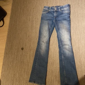 Blå bootcut jeans - Säljer ett par snygga blå bootcut jeans i bra skick. De har en klassisk femficksdesign med knappar och dragkedja fram. Perfekta för både vardag och fest! Passar bra till en avslappnad stil eller med klackar för en mer dressad look.