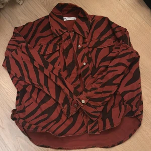 Röd och svart zebramönstrad jacka - Säljer en cool röd och svart zebramönstrad jacka från Zara. Skjortan har långa ärmar och knappar framtill. Perfekt för en djärv look på festen eller en utekväll. Den är i bra skick och redo att bäras av någon med stil! 🖤❤️