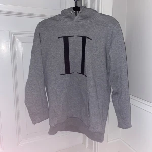 Grå hoodie med svart tryck - Säljer en snygg grå hoodie med ett coolt svart tryck på framsidan. Perfekt för både höst och vår. Den har en klassisk känguruficka och en bekväm huva. Passar perfekt för en avslappnad stil eller när du bara vill mysa hemma. Hör av dig vid intresse!
