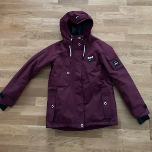 Vinröd jacka från Dope - Säljer en snygg vinröd skidjacka från Dope i storlek XS. Jackan har flera fickor med knappar. Perfekt för höst och vinter med sitt tåliga material och stilrena design. Passar både till vardags och utomhusaktiviteter.