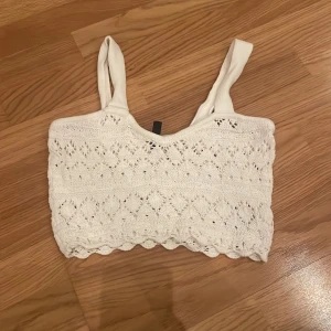 Vit stickad linnetopp - Säljer en superfin vit stickad linnetopp med ett vackert hålmönster. Toppen är ärmlös och har breda axelband, perfekt för sommardagar. Den är croppad och ger en söt och avslappnad look. Passar perfekt till jeans eller kjol för en casual stil.