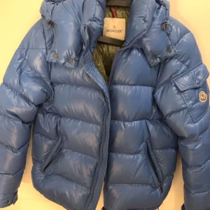 Moncler Maya Blue - Säljer en snygg blå pufferjacka från Moncler i mycket bra skick. Jackan har en quiltad design med dragkedja och en praktisk huva. Perfekt för kalla vinterdagar! Den har också en cool ficka med Moncler-loggan på ärmen. Passar både för vardag och lite finare tillfällen. Jackan är en limited edition modell så den säljs inte längre. Nypris 18500 kr storlek 2