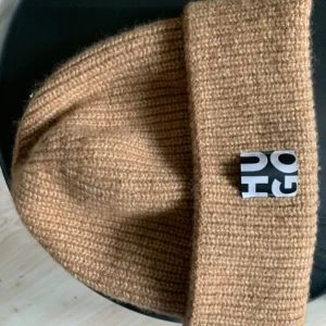 Beige stickad mössa Hugo Boss - Säljer en snygg beige stickad mössa i nytt skick. Den är perfekt för höst och vinter och har en stilren design med en liten etikett framtill. Mössan är mjuk och bekväm, perfekt för att hålla dig varm under kyliga dagar.