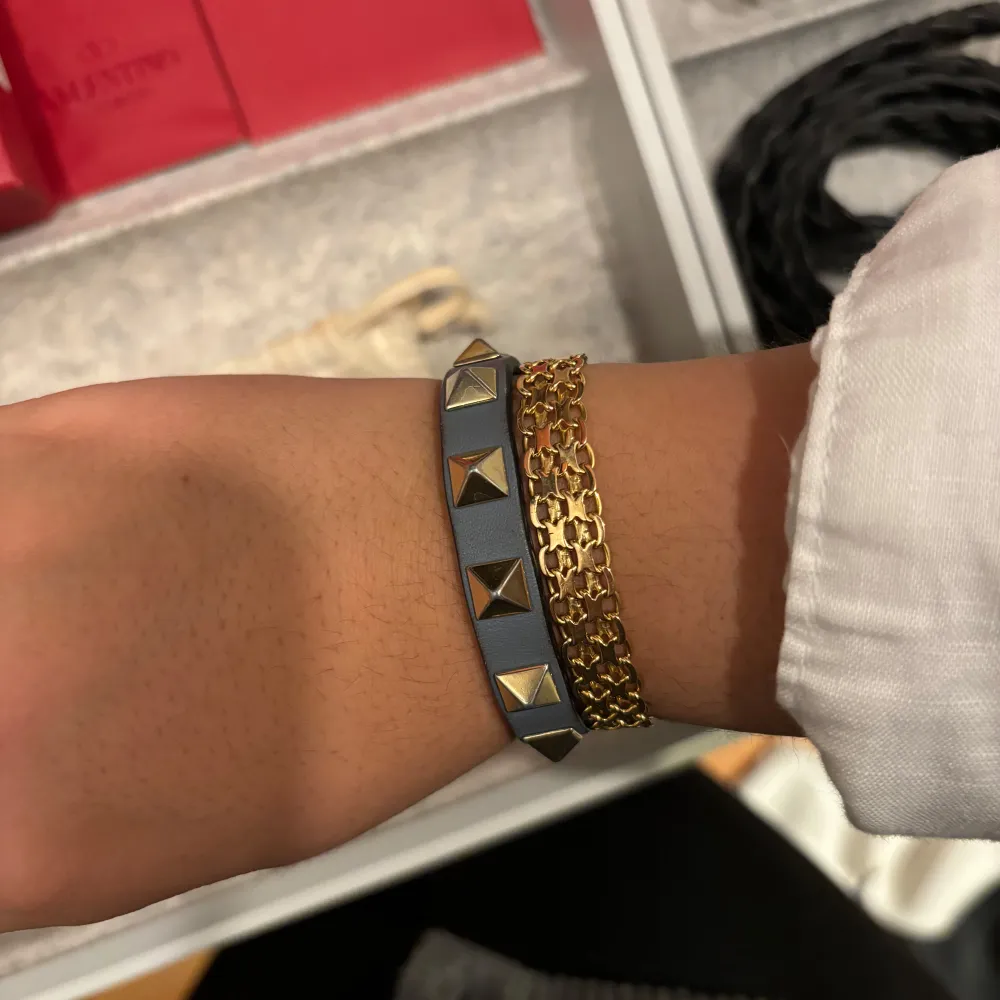 Säljer ett snyggt blått armband från Valentino med guldiga pyramidnitar. Armbandet är i mycket bra skick och kommer med originalförpackning och dustbag samt 1 extra nit. Det finns en liten defekt på armbandet som går att se på sista bilden. Perfekt accessoar för att ge din outfit en edgy touch! 🖤. Accessoarer.