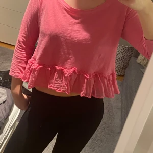 Rosa blus med volangdetaljer - Säljer en söt rosa blus med volangdetaljer i nederkant. Blusen har långa ärmar och knappar på baksidan. Perfekt för vår och sommar!