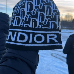 Svart och vit mössa från Dior - Snygg svart och vit mössa från Dior med ett coolt mönster och logga. Perfekt för att hålla sig varm och stilren under vintern. Tillverkad i en blandning av bomull och akryl för extra komfort.