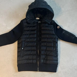Svart cardigan från Moncler - Säljer en snygg svart jacka från Moncler i helt ny skick. Jackan har en quiltad framsida med dragkedja och en mysig huva. Ärmarna och ryggen är stickade vilket ger en cool kontrast. Perfekt för höst och vår! Jackan är köpt förra året i Moncler i Milano. Kvitto plus regristrering av jackan tillkommer även vid seriösa skrivare. Nypris 12 045. Och slut i alla moncler affärer i Sverige. 