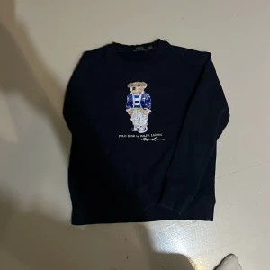 Ralph Lauren tröja - Säljer en svart tröja från Ralph Lauren med den ikoniska Polo Bear på framsidan. Tröjan är i bra skick och har långa ärmar. Den är liten i storleken så är mer storlek M. Hör av er vid frågor eller bud🤩👍