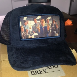 Velvet keps marinblå - Stilren ny (nästan ny) velvet keps från Brevado med ett unikt tryck av en grupp människor som gör peace-tecken. Kepsen har ett nätmaterial på baksidan för bättre ventilation och en justerbar rem för perfekt passform. Perfekt för en avslappnad stil eller som statement piece!