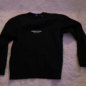 Svart tröja från Jack & Jones - Säljer en svart tröja från Jack & Jones Originals. Den har en enkel design med texten 'Originals Studio' på bröstet. Perfekt för en casual look och passar till det mesta. Tröjan är i bra skick och redo för nya äventyr! Köptes för för 1400 men används inte