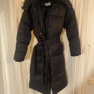 Svart dunjacka från NA-KD - Säljer en svart lång dunjacka från NA-KD i mycket bra skick. Jackan har ett bälte i midjan för en mer figursydd look, aldrig använt utan fick i present och säljer nu eftersom den inte kommer till användning. Den är jätte varm och perfekt nu till vintern. För fler bilder skriv privat🩷 pris kan diskuteras