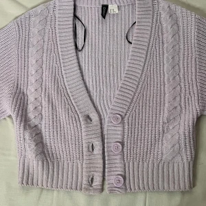 Ljuslila stickad kofta - Superfin ljuslila stickad kofta från HM i storlek XXS. Den är croppad med flätstickade detaljer och har en v-ringad design med knappar framtill. Perfekt för vår och sommar! 💜