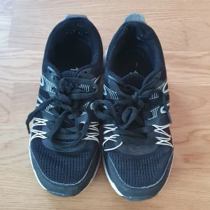 Svarta sneakers med vita detaljer - Säljer ett par svarta sneakers i bra skick med vita detaljer och snörning. Perfekta för vardagsbruk eller träning. De har en bekväm passform och är lätta att matcha med olika outfits.