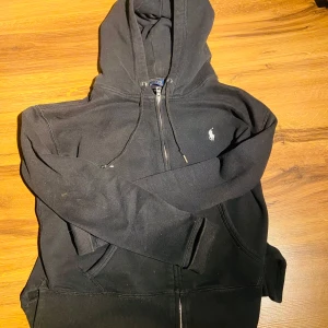 Svart hoodie från Polo Ralph Lauren XS - Säljer en svart hoodie från Polo Ralph Lauren i bra skick. Den har en dragkedja framtill och den klassiska broderade loggan på bröstet. Perfekt för höst och vinter, och passar till både vardag och träning. Superbekväm och stilren! Öppen för alla prisförslag! 