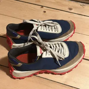 Säljer ett par snygga sneakers från Camper i blått och rött. Skorna har en cool design med vita och beige detaljer samt en robust röd sula. Perfekta för både vardag och äventyr! De har snörning för en bra passform och är i bra skick.