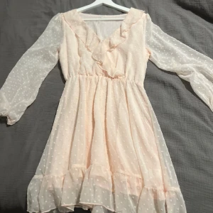 Ljusrosa klänning med volangdetaljer - Säljer en superfin ljusrosa klänning med volangdetaljer och prickigt mönster. Den har långa, genomskinliga ärmar och en söt volangkant vid halsen och fållen. Perfekt för vår och sommar! 🌸