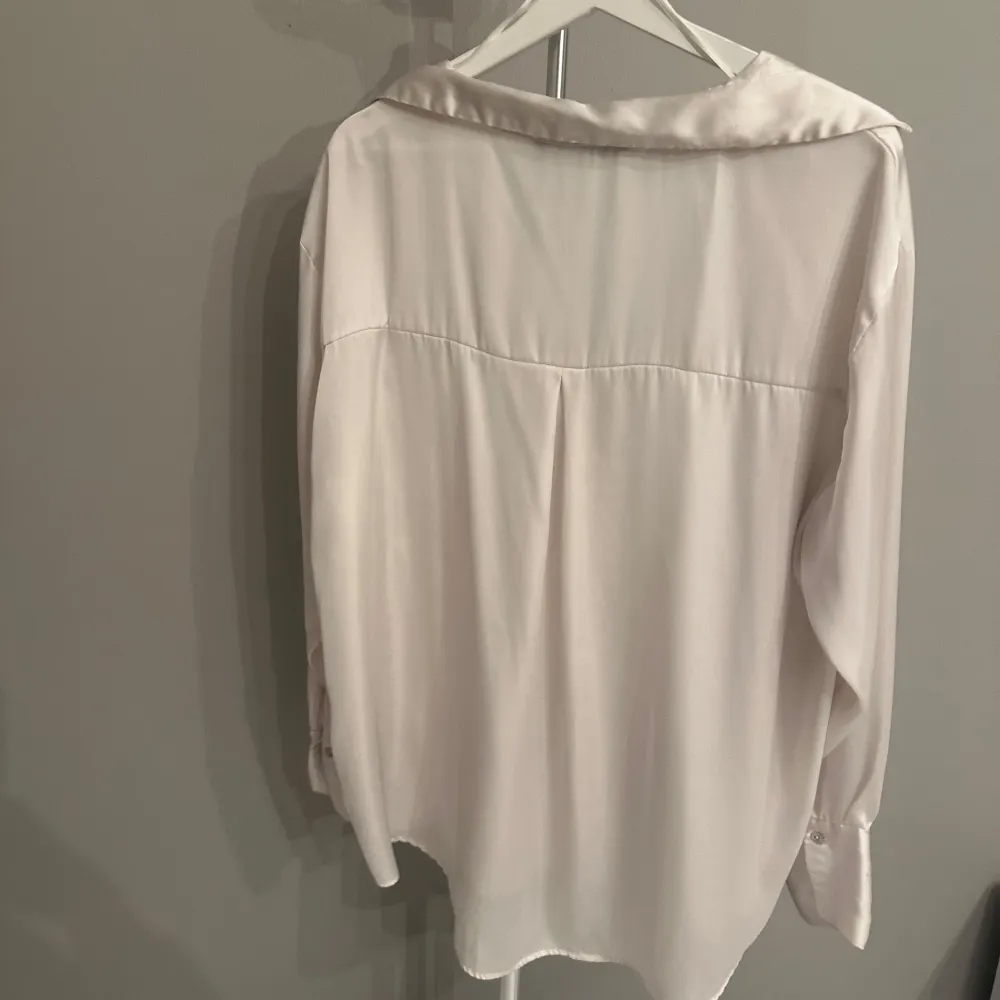 Säljer en elegant vit blus från Zara i storlek XXL. Blusen har en lös passform med långa ärmar och knappar framtill. Perfekt för både vardag och festliga tillfällen. Materialet känns mjukt och lyxigt, vilket ger en skön känsla mot huden. Passar utmärkt till både jeans och kjol! I silkes liknande material. Blusar.