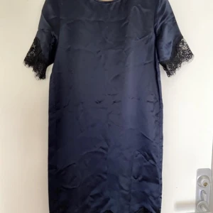 Mörkblå klänning från Samsøe Samsøe - Snygg knälång mörkblå klänning från Samsøe Samsøe i storlek XS. Den har korta ärmar med spetsdetaljer som ger en elegant touch. Perfekt för både vardag och festliga tillfällen. Materialet känns lyxigt och bekvämt.