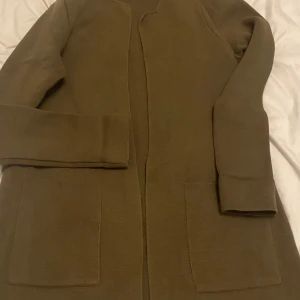Olivgrön cardigan  - Säljer en stilren olivgrön cardigan i mycket bra skick. Den har en enkel design med långa ärmar och två stora fickor framtill. Perfekt för höst och vår, och passar både till vardags och lite finare tillfällen.