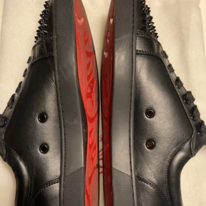 Svarta sneakers med nitar från Christian Louboutin - Säljer ett par svarta sneakers i skinn från Christian Louboutin. De har en cool design med nitar på tån och en ikonisk röd sula. Perfekta för att ge din outfit en edgy touch. Skorna är i nytt skick och kommer i originalförpackning.