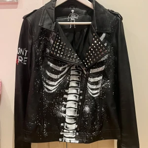 Svart skinnjacka med skelettmotiv från Full Volume by EMP - Cool svart skinnjacka (fakeläder) med ett unikt skelettmotiv i vitt och röda detaljer. Jackan har nitar på kragen och en dragkedja framtill. Aldrig använd! Säljer för att den va för lite skulle säga att den är i storlek S/XS men står tyvärr inte. Tycker om den jättemycket och hoppas att den kan få ett nytt hem där den faktist blir använd xd Har katter hemma men jackan har legat nerpackas så borde inte vara ett problem vid allergi!