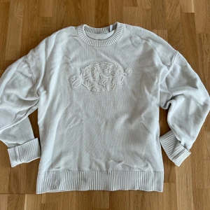 Vit stickad tröja från Weekday - Vit stickad tröja från Weekday. Den har ett coolt broderat mönster på framsidan och ribbade muddar vid ärmslut och nederkant. Perfekt för en stilren vinter. Passar både till vardags och fest!